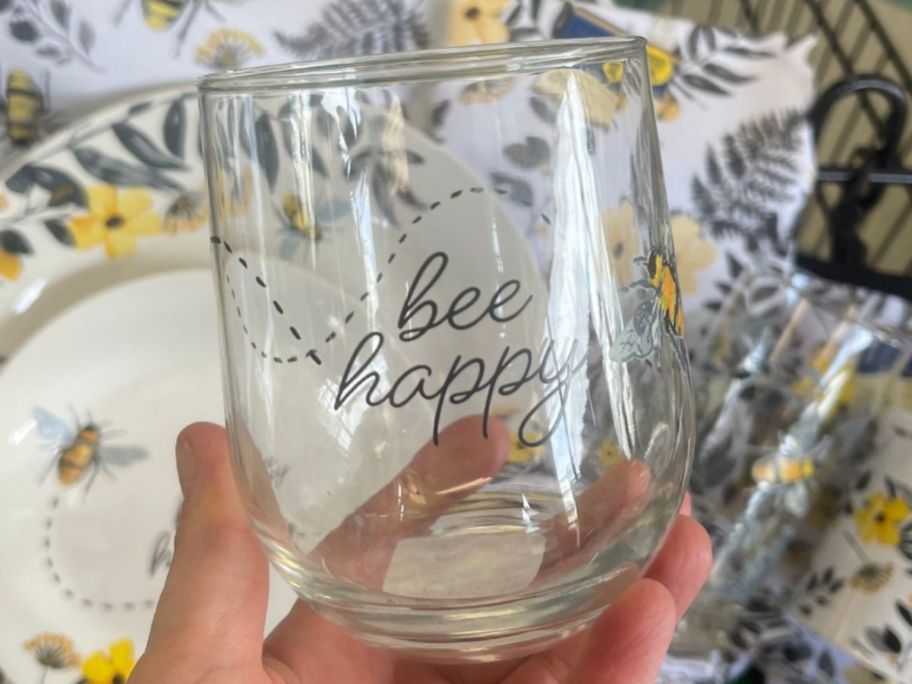 Hand holding up a Bee Happy Dollar Tree Stemless Wine Glass
