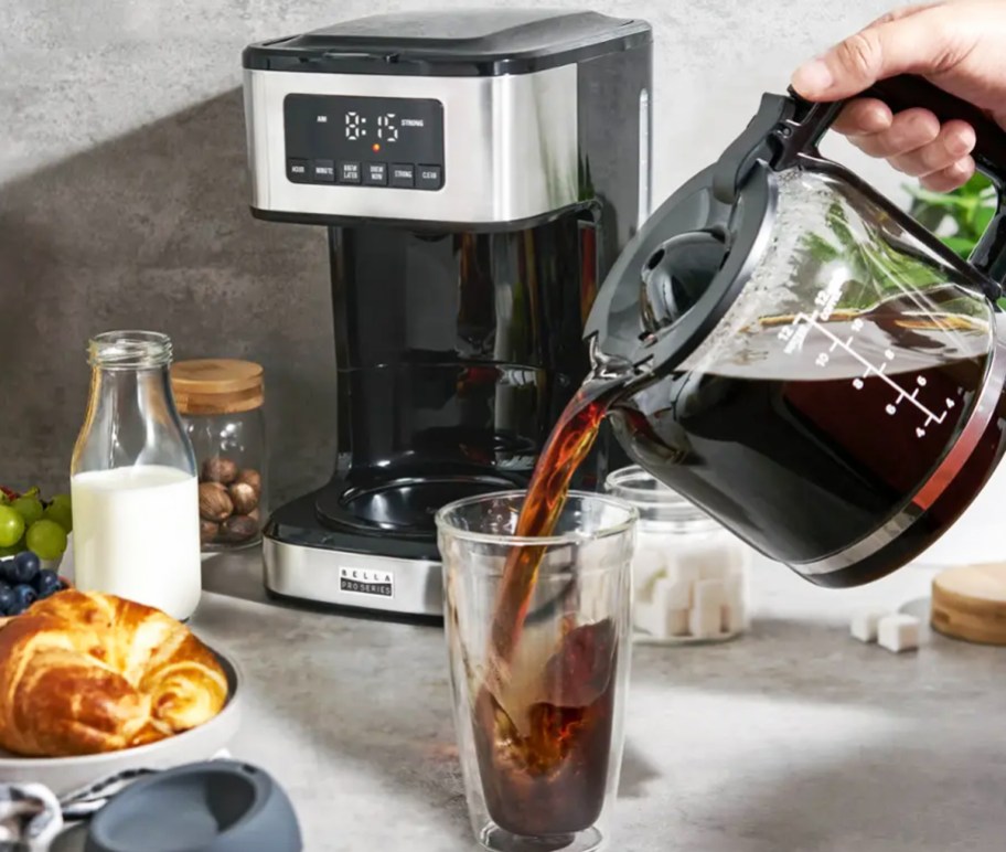 pouring a cup of coffee in front of a stainless steel coffee maker