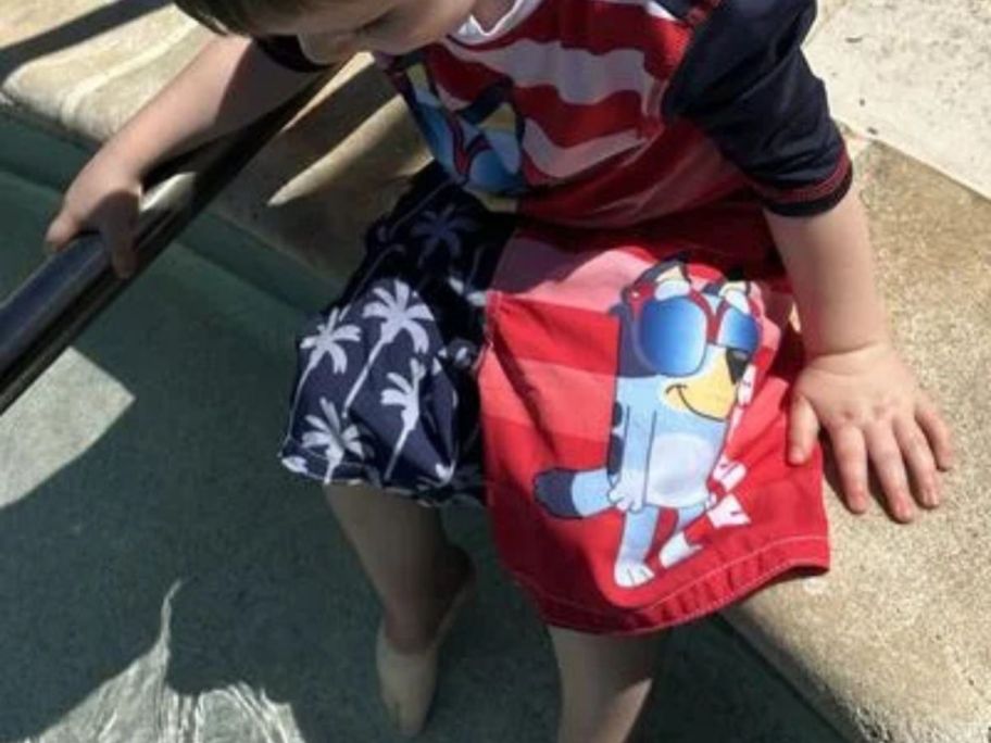 A boy in a pool wearing Bluey swim shorts