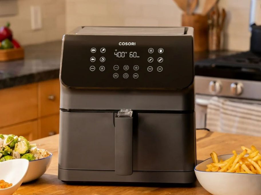 A dark gray air fryer on a countertop in a kitchen surrounded by food