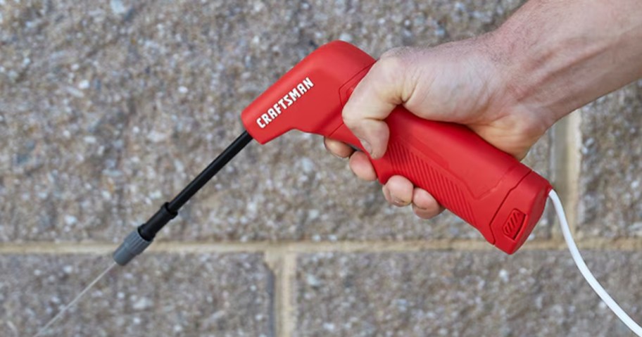 A person using a red CRAFTSMAN battery-powered sprayer to spray liquid near a wall.