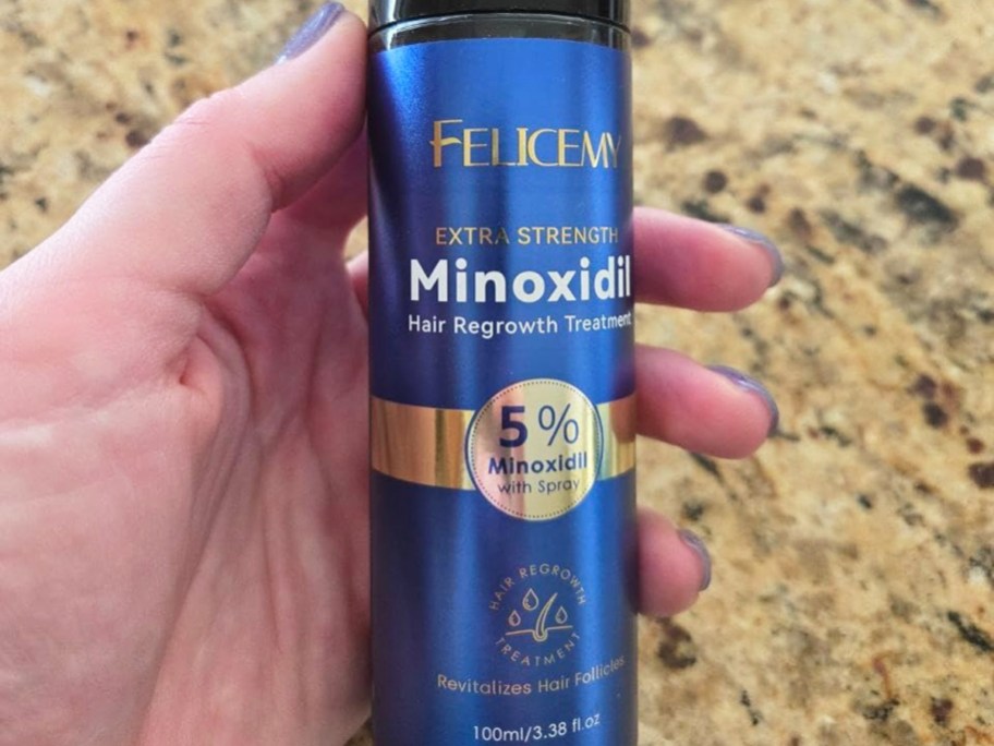 hand holding a blue can of Felicemy Minoxidil Hair Growth Treatment spray