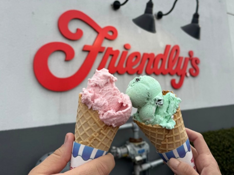 holding two ice cream cones in front of a Friendly's restaurant
