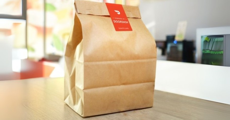 a brown bag with food in it with a DoorDash delivery sticker sitting on a restaurant counter