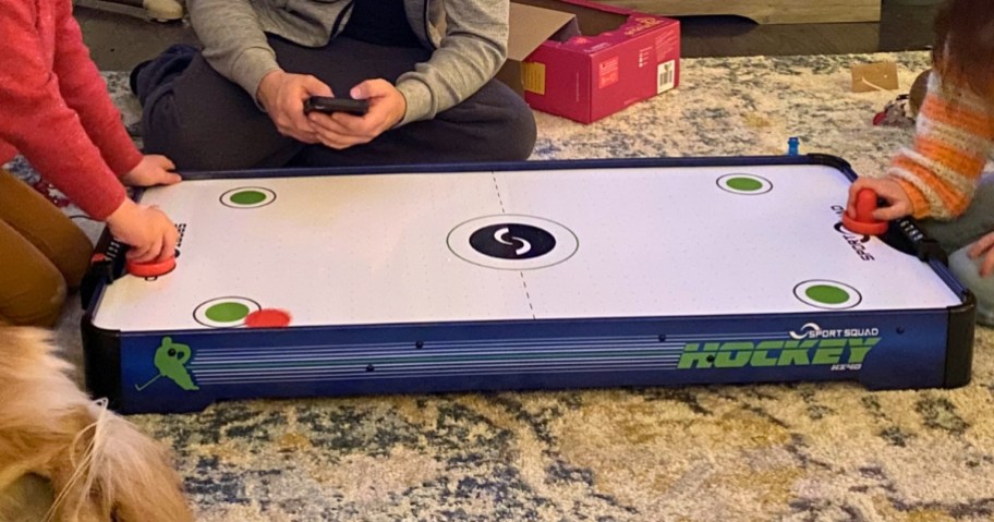 famiily playing with a table top air hockey table on the floor in a living room