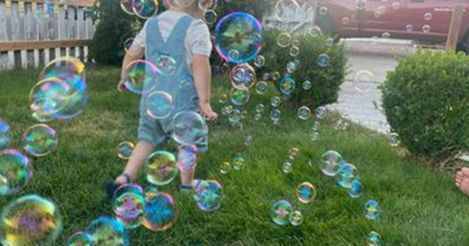 little boy walking thru a bunch of bubbles in a yard