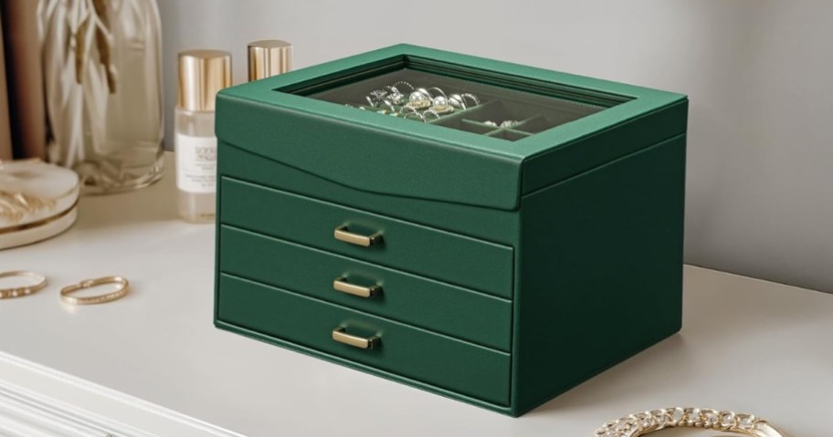 a large green jewelry box with 3 drawers and a glass top on a dresser