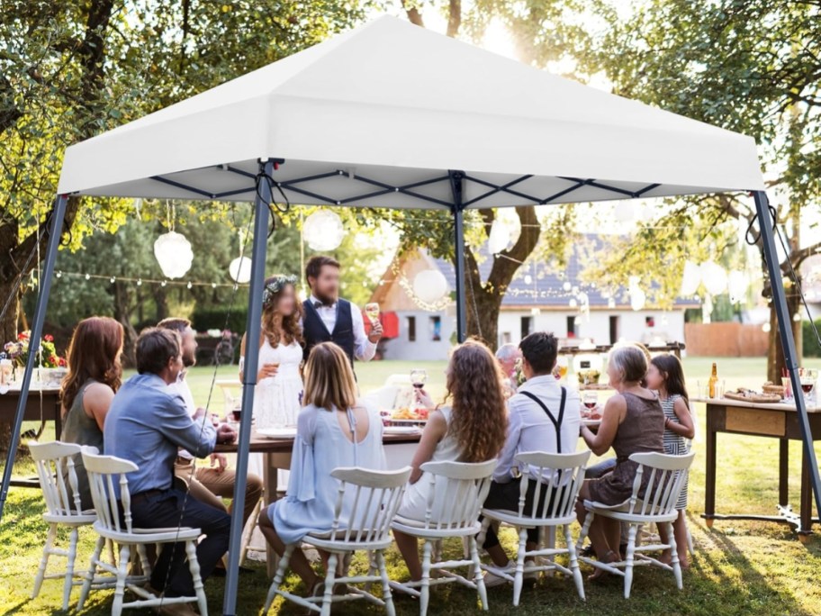 people eating at a table under a white pop up canopy tent outdoors