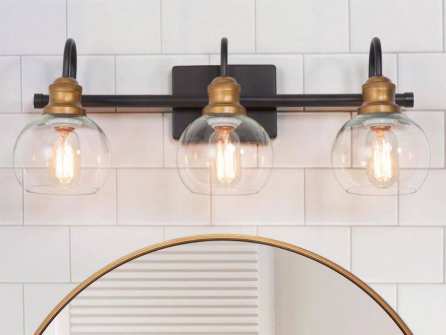A LNC 22.5" 3-Light Modern Aged Brass & Black Vanity Light over a mirror