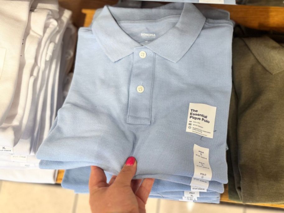 Hand grabbing a folded Sonoma Goods for Life Men's Polo Shirt from a stack of shirts at the store