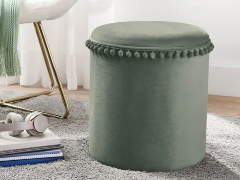 A green ottoman with pom poms around the top in a child's room