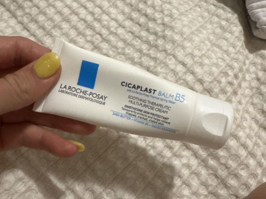 A person holding a white tube of La Roche Cicaplast Baume B5