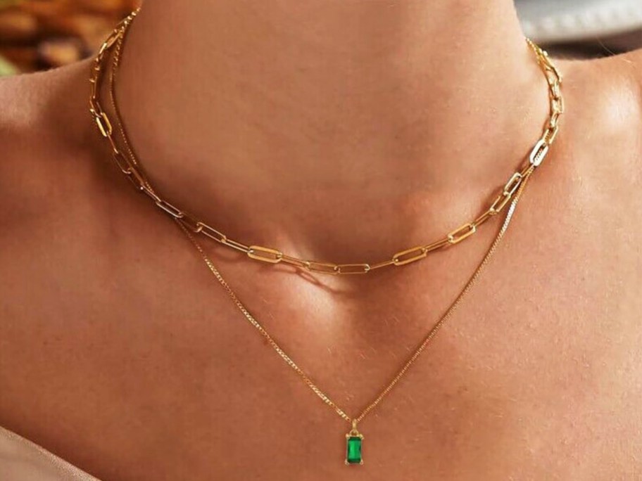 woman wearing a layered necklace with emerald pendant 