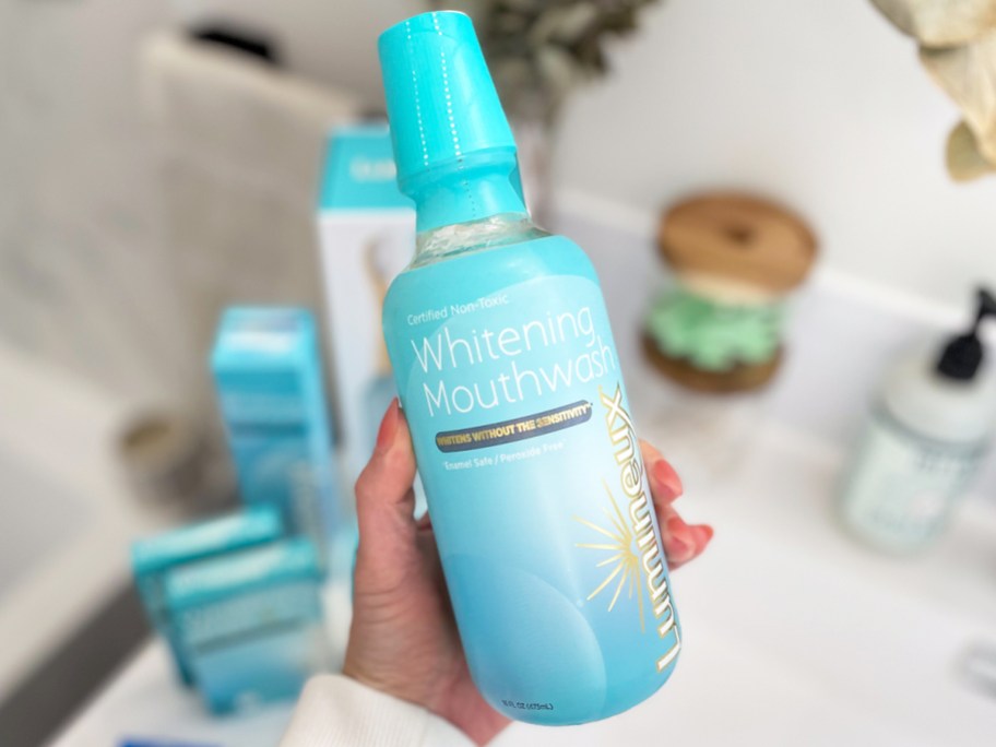hand holding bottle of Lumineux Whitening Mouthwash above bathroom counter