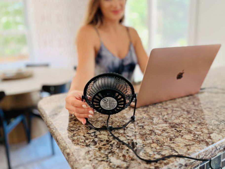 A woman working on a computer is being cooled down by a 4" personal fan. 