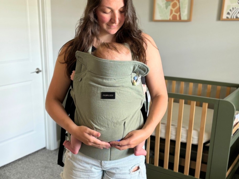 woman with a baby in a green baby carrier in a nursery