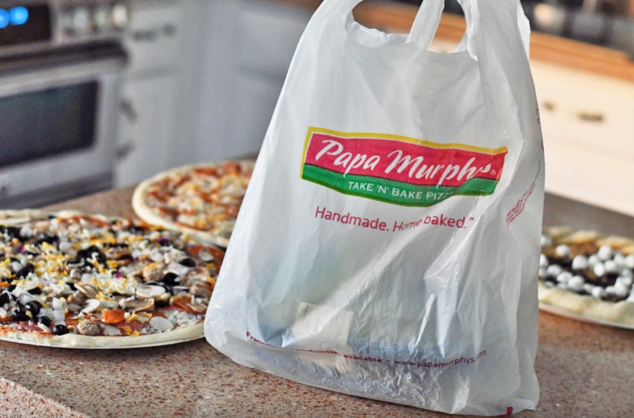 Papa Murphy’s bag on kitchen counter in front of multiple pizzas