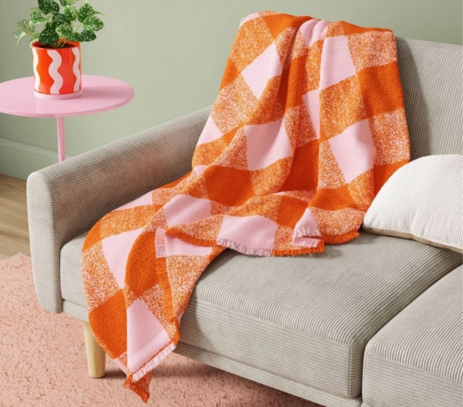 a pink and orange plaid check throw blanket drapde over the corner of a sofa