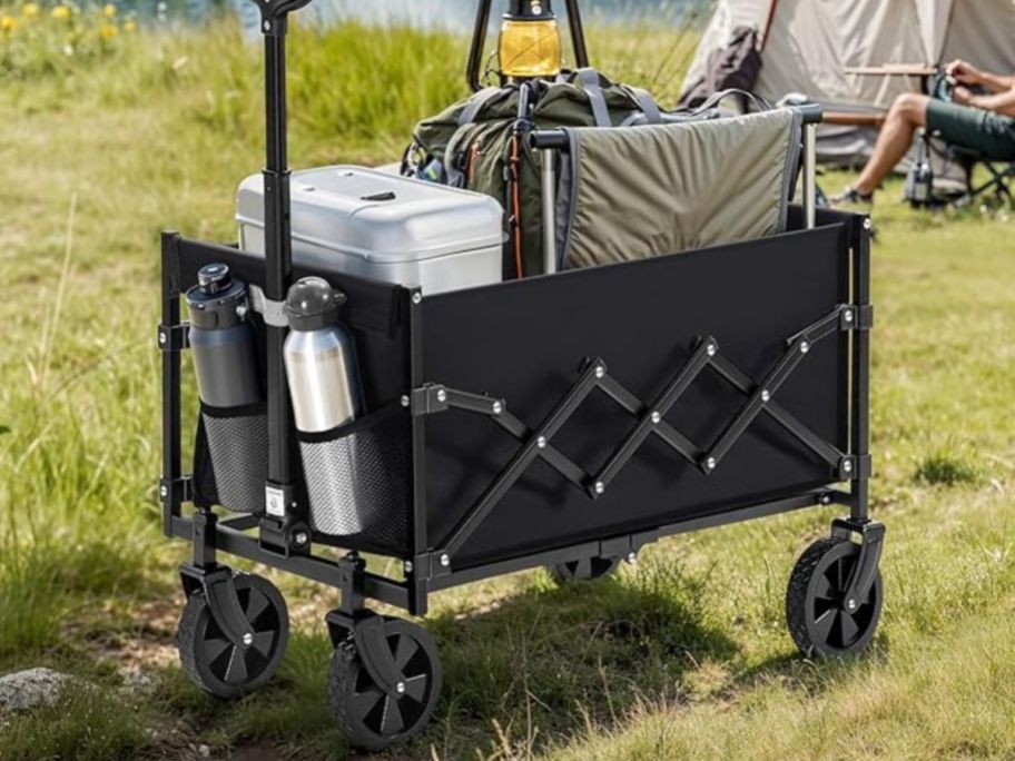 A black, collapsible wagon made of fabric, in a field near a campsite
