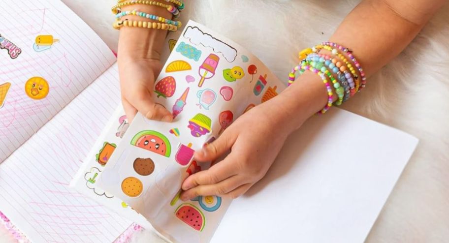 Girl playing with stickers while having her arms with tons of fun bracelets