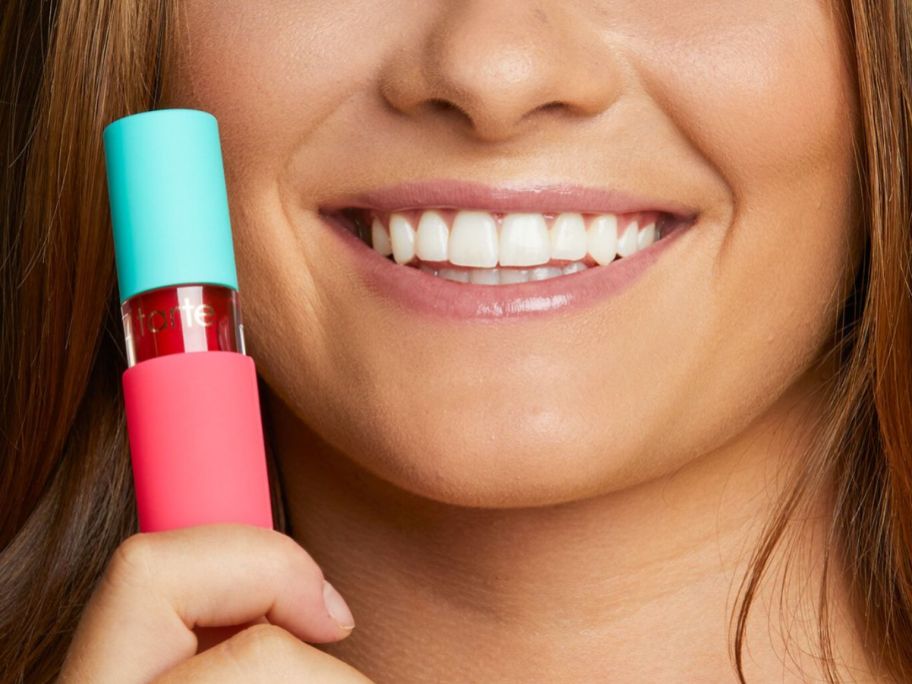 Woman holding a Tarte Sugar Rush Lip Sip Oil next to her mouth
