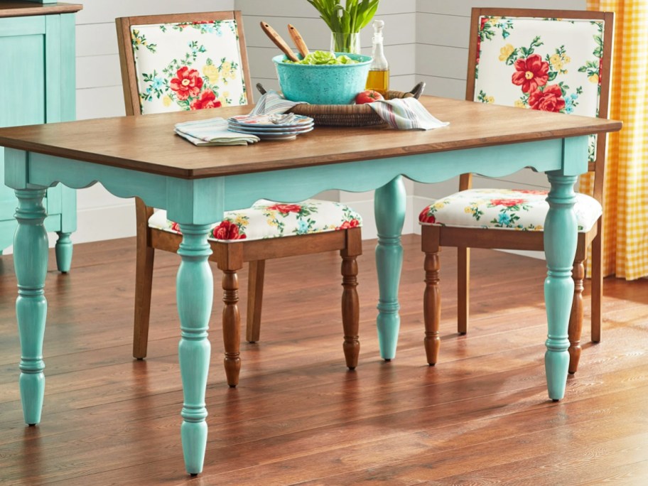 teal dining table with wood top and floral print chairs around it