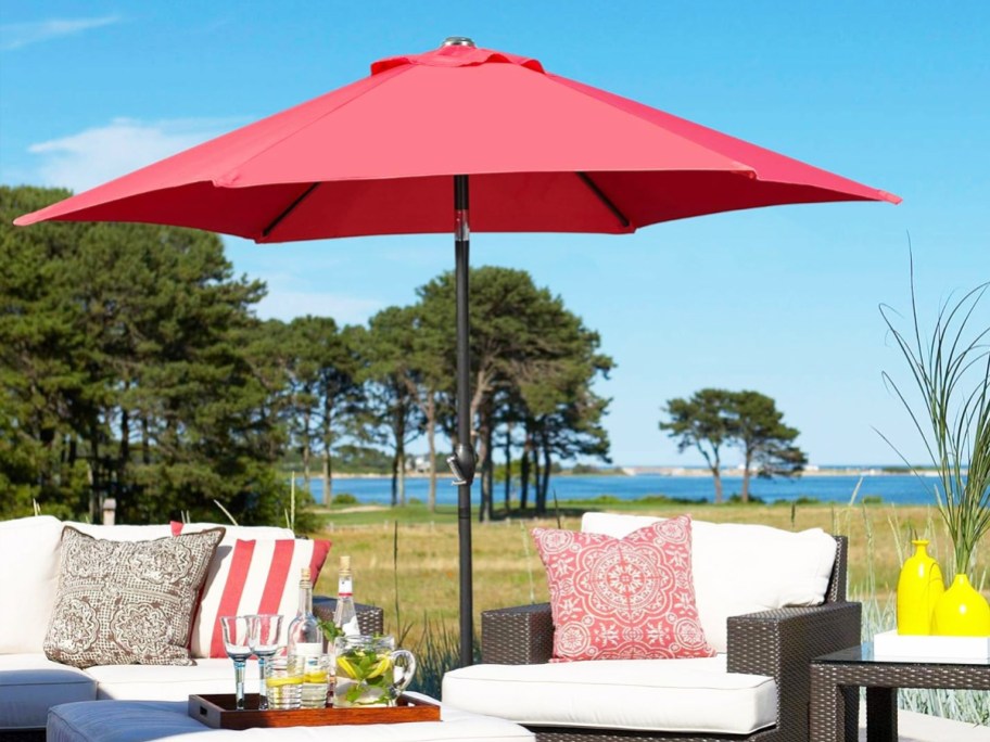 red patio umbrella over a patio set with white cushions