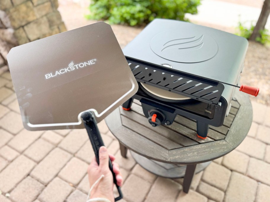 hand holding pizza peel over blackstone pizza oven