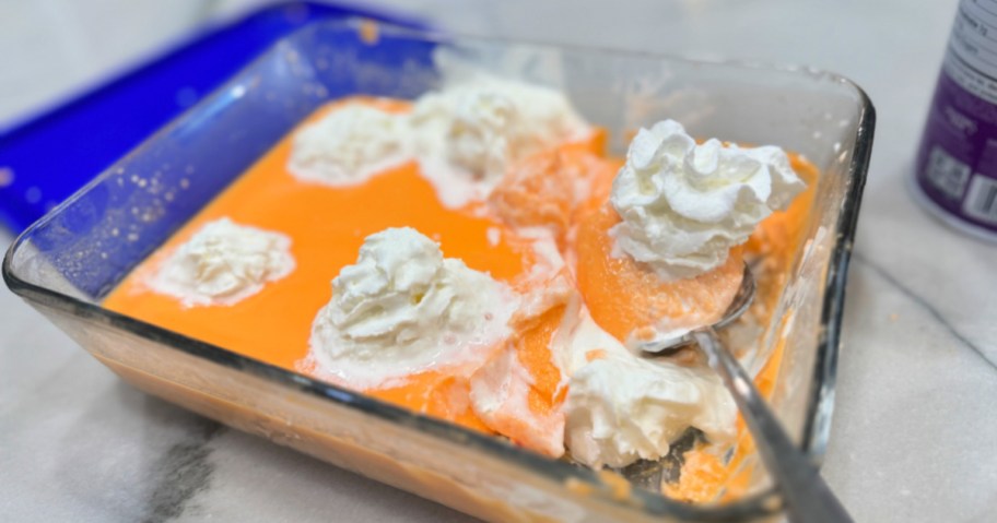 glass container with orange protein jello and whipped cream 