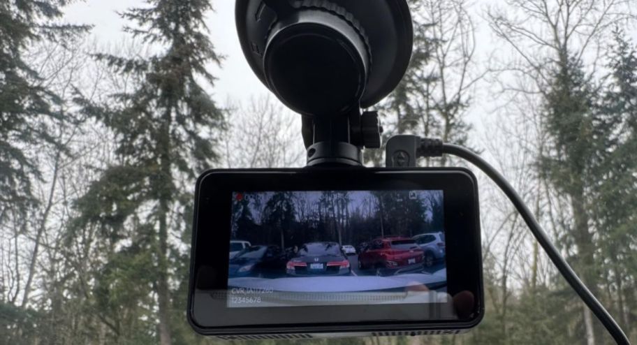 Black dashcam displayed on the windshield of a car showing a few cars