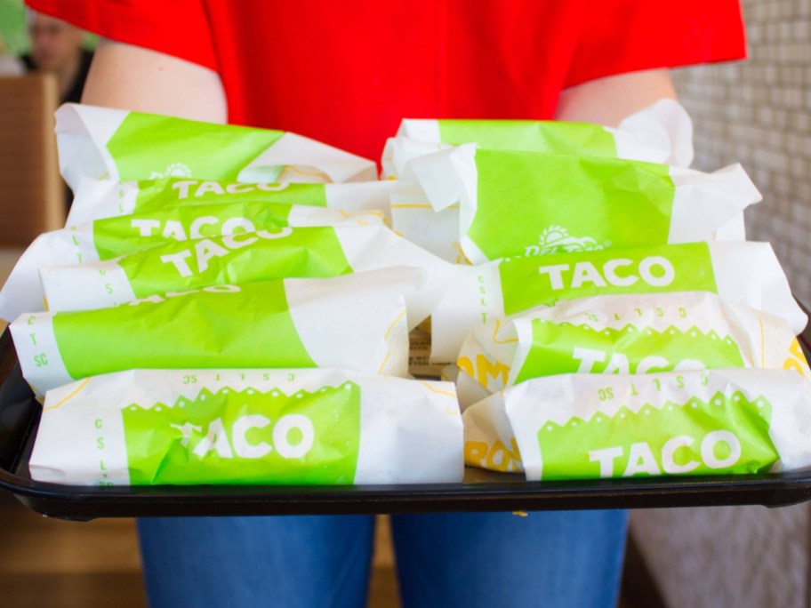 holding a tray of wrapped tacos
