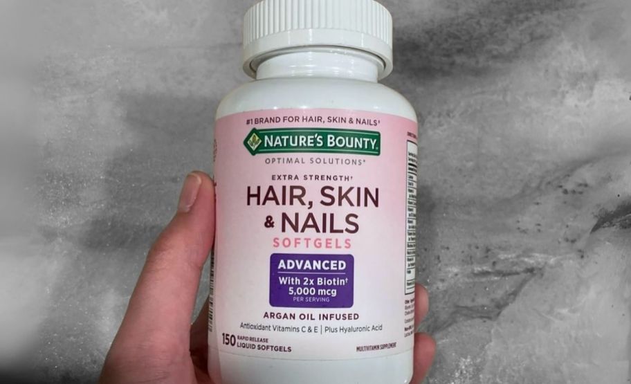 a womans hand holding a bottle of hair skin and nail supplements