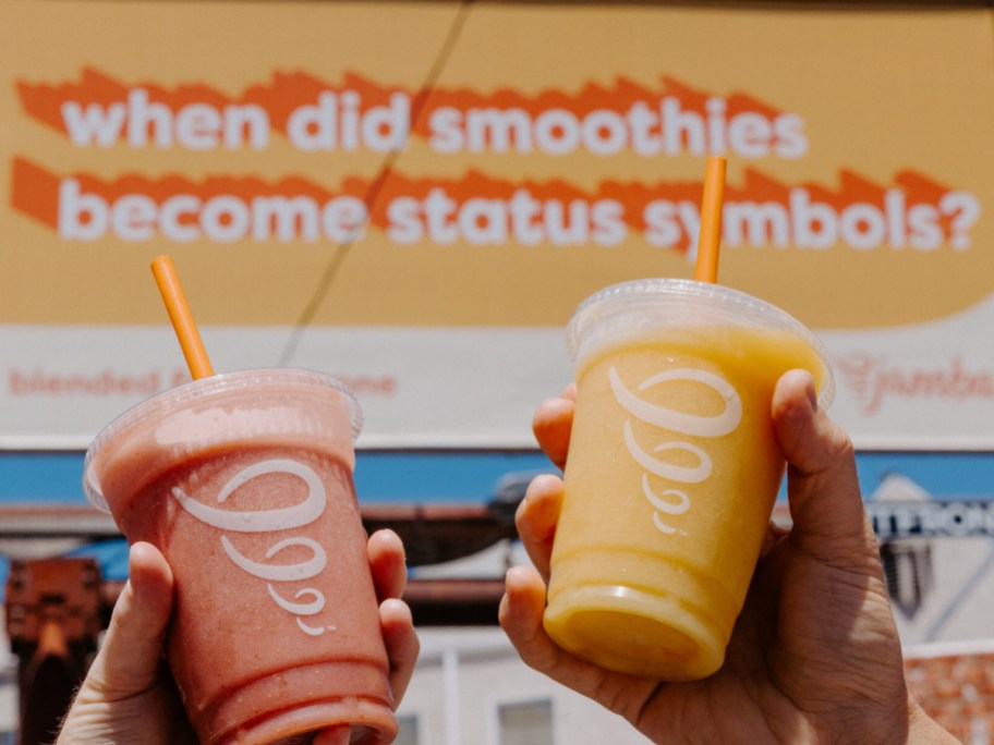 holding 2 smoothies in front of a billboard