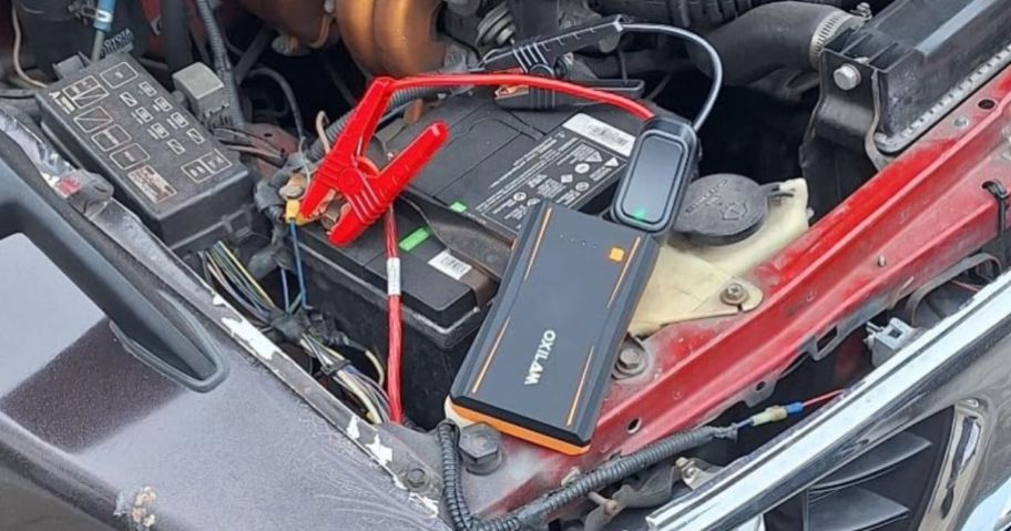 OXILAM Portable Jump Starter hooked up to battery in hood of car