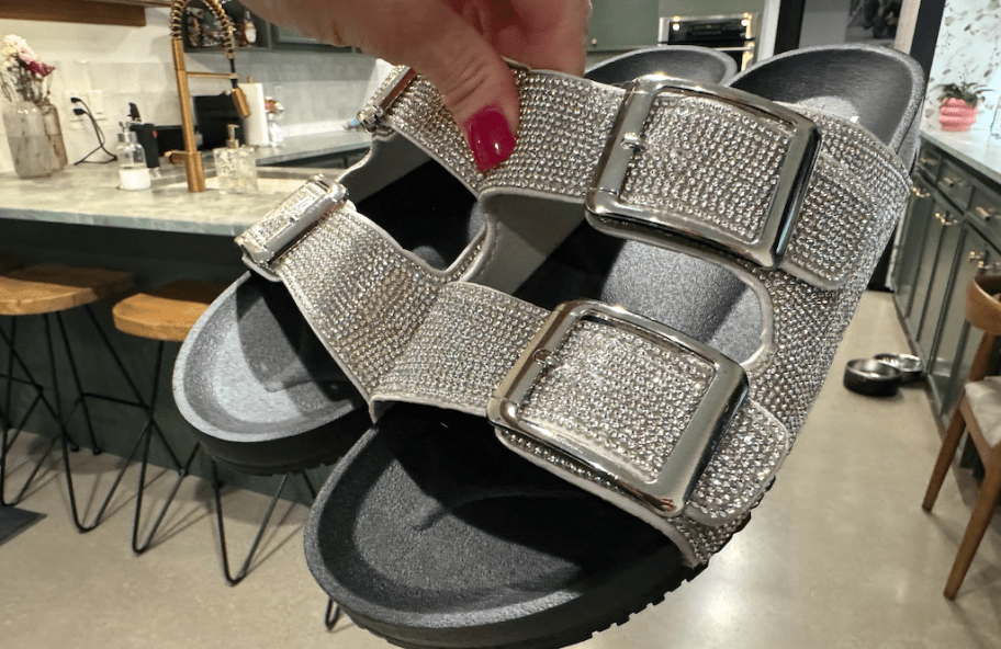 woman's hand holding a pair of black footbed sandals with silver sparkle straps