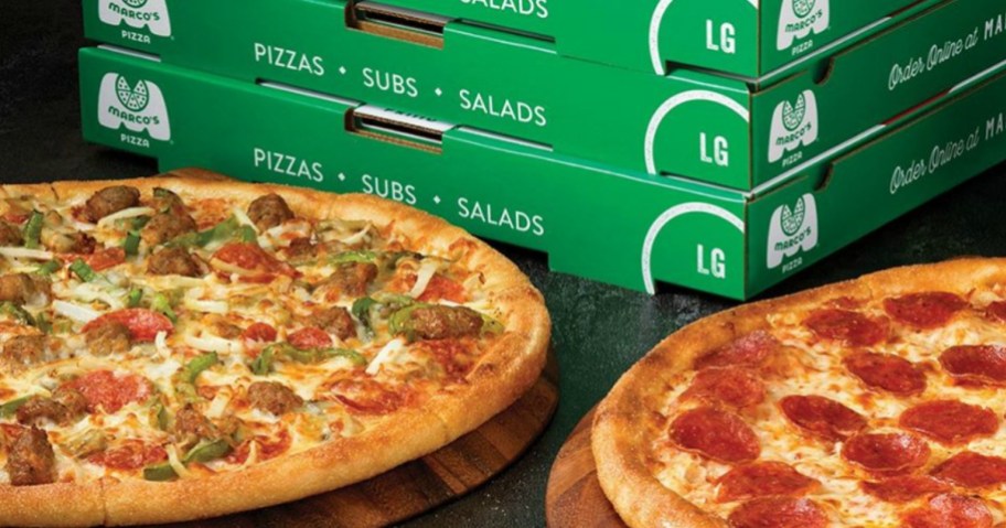 two pizzas in front of a stack of pizza boxes