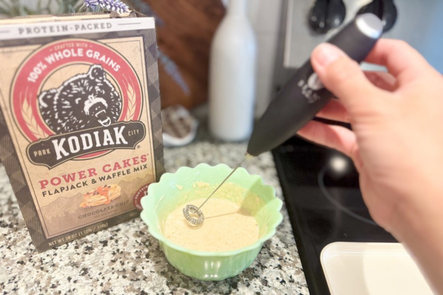 hand putting milk frother into pancake batter in green bowl