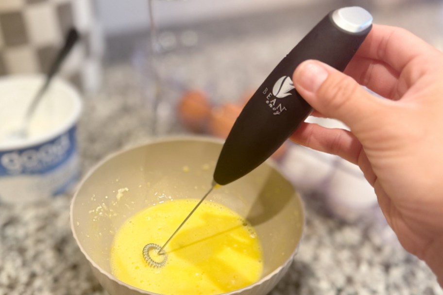 hand holding milk frother in egg bowl