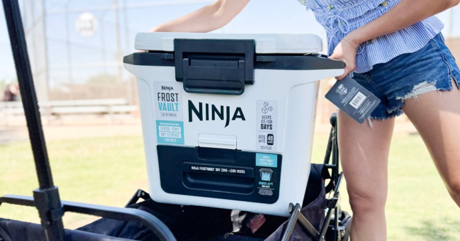 person holding white ninja cooler above wagon 