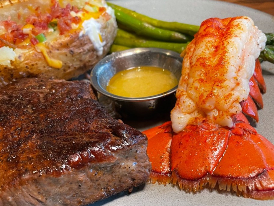 lobster on plate next to steak, butter, and baked potato