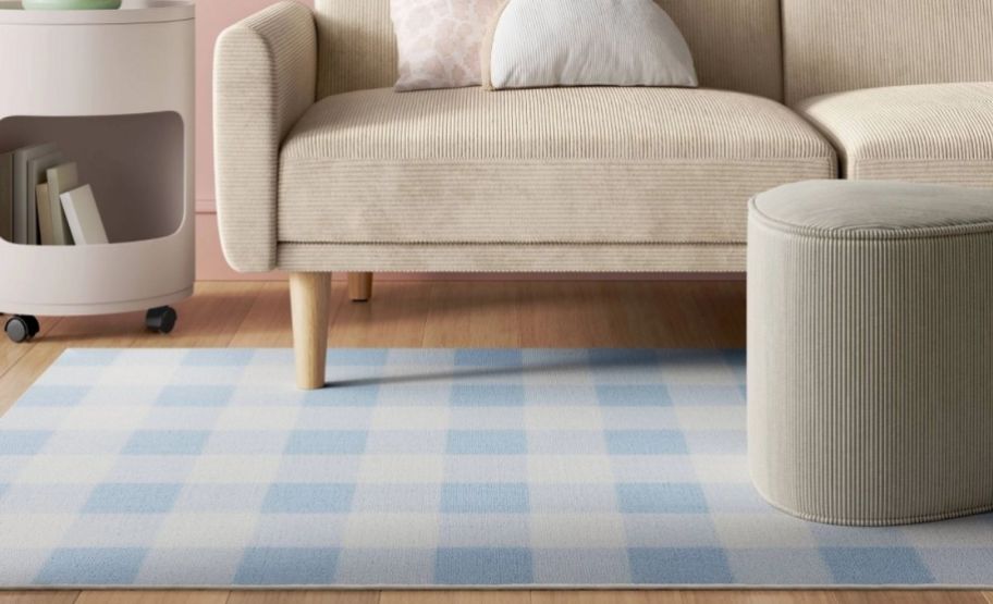 a blue and white gingham rug on a floor shown with a poof, sofa and end table