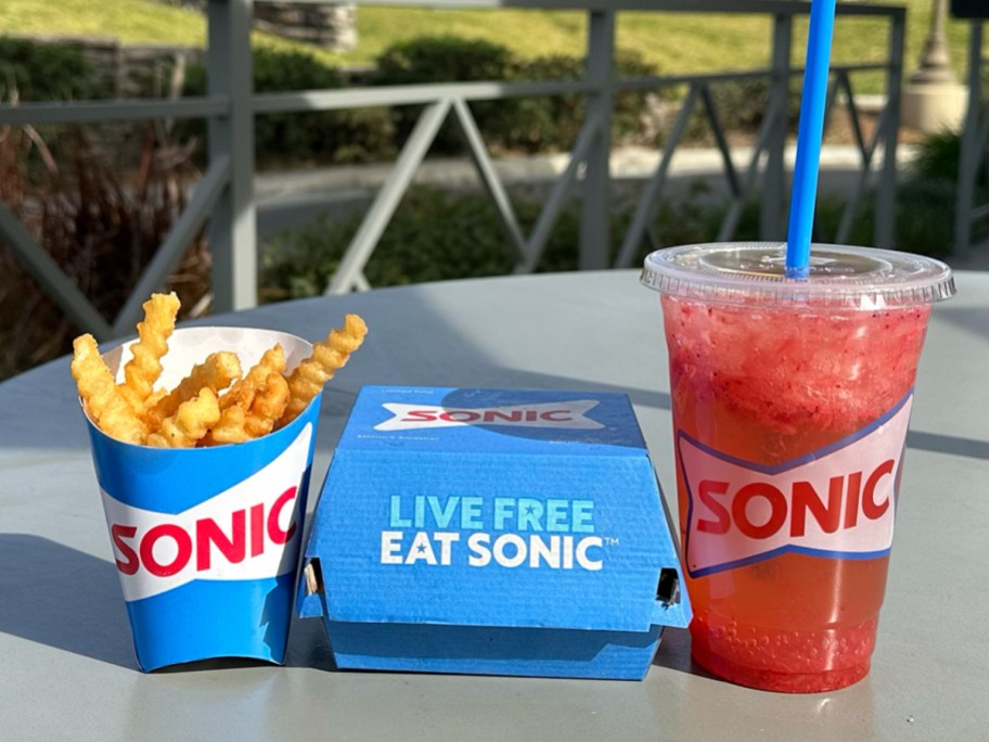 fries, a burger carton, and a red slushie from Sonic on a table outdoors