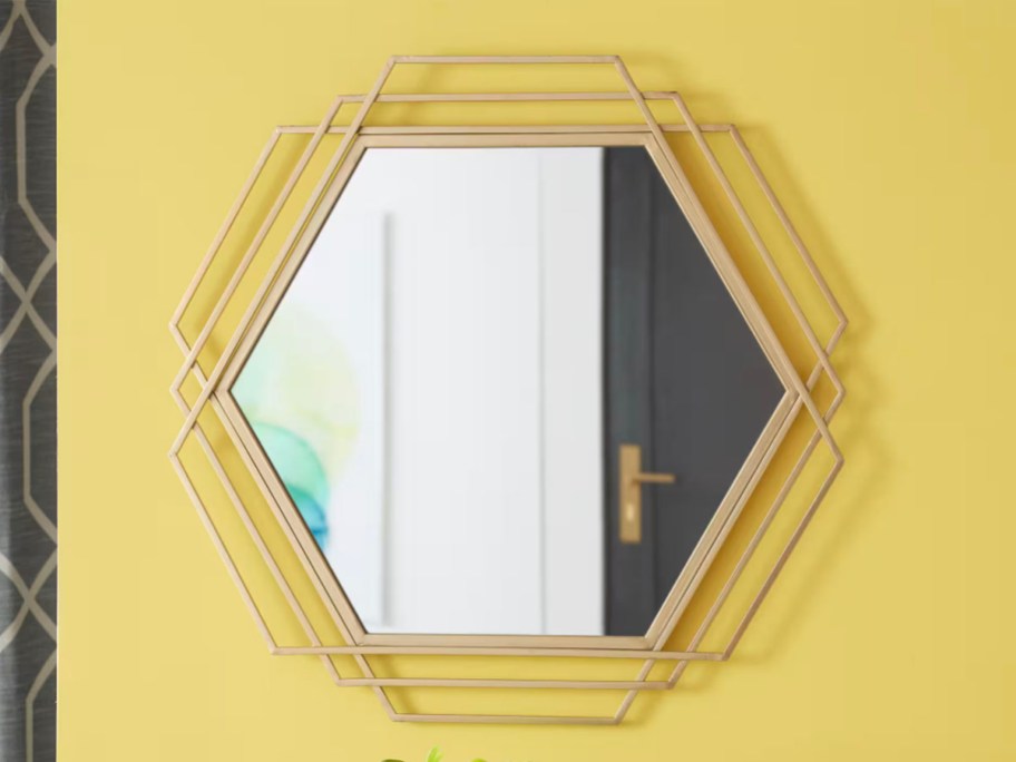 hexagonal gold mirror hanging on yellow wall 