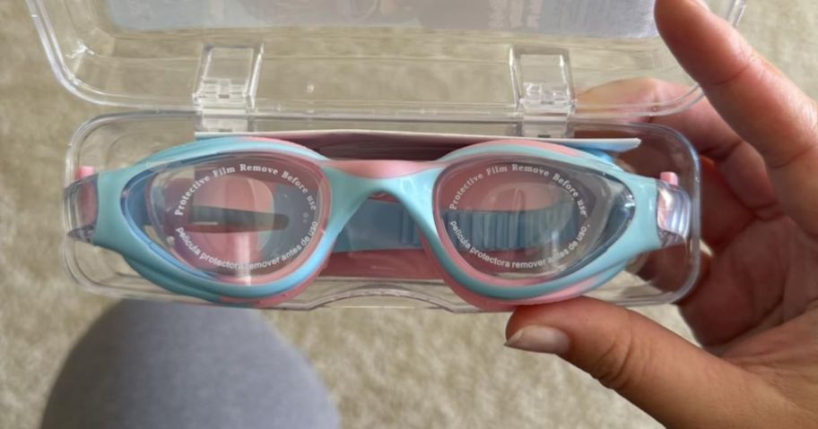 hand holding blue and pink kids swim goggles in case