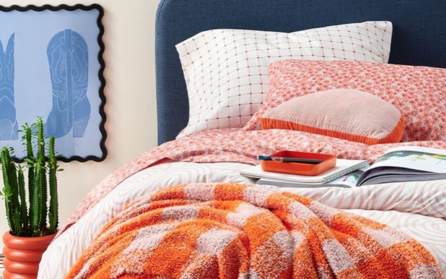 a bed shown made with coordinating, pillows, duvet, throwblanket, and sheets along with coordinating decor items including graphic prints