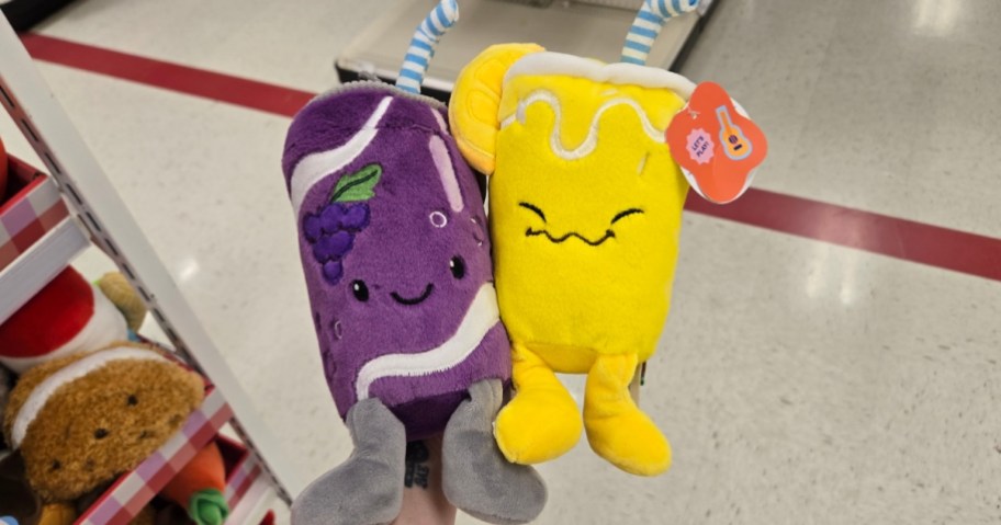 hand holding a grape soda plush and a lemonade plush