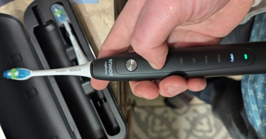 black Auraglow Electric Toothbrush in hand above case with extra brush head