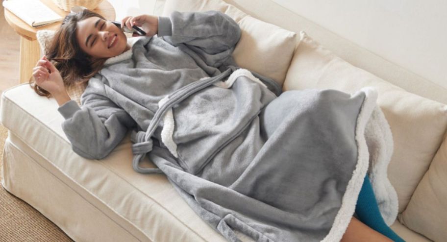 woman laying on a couch wearing a hoodie blanket while speaking on the phone