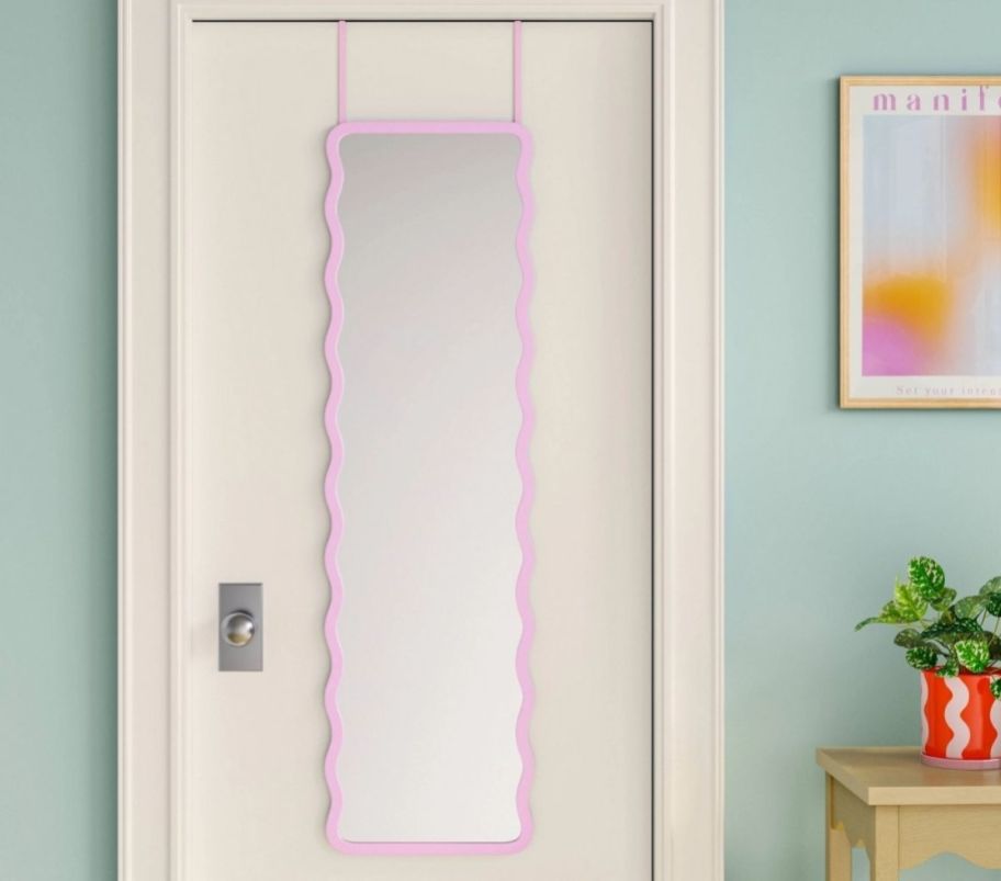 a pink framed wavy mirror on the back of a door