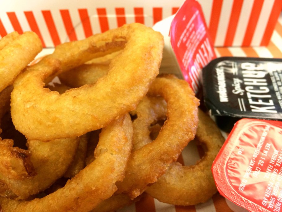 onion rings in a paper carton next to dipping sauces